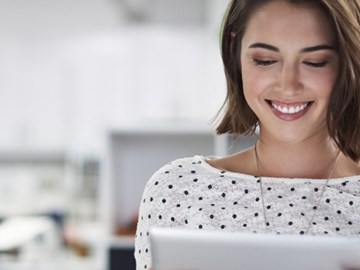 Fragen zu Produktem Eine Frau sitzt im Büro und hält ein Tablet in der Hand, während sie lacht
