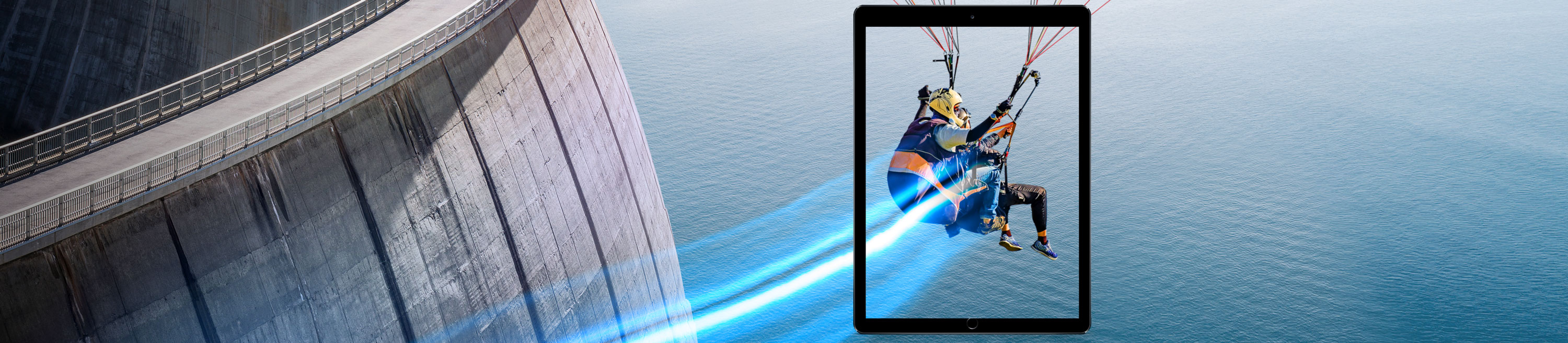 Zwei Personen fliegen mit einem Gleitschirm vor einer Staumauer