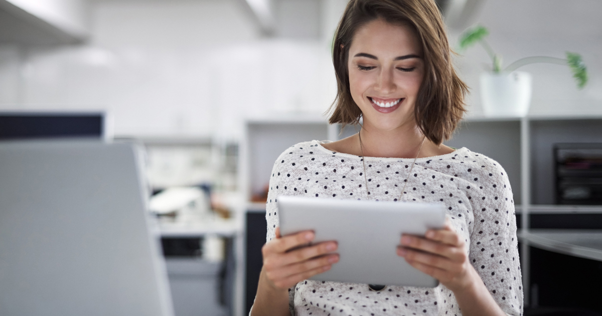 Eine Frau sitzt im Büro und hält ein Tablet in der Hand, während sie lacht