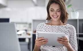Fragen zu Produktem Eine Frau sitzt im Büro und hält ein Tablet in der Hand, während sie lacht