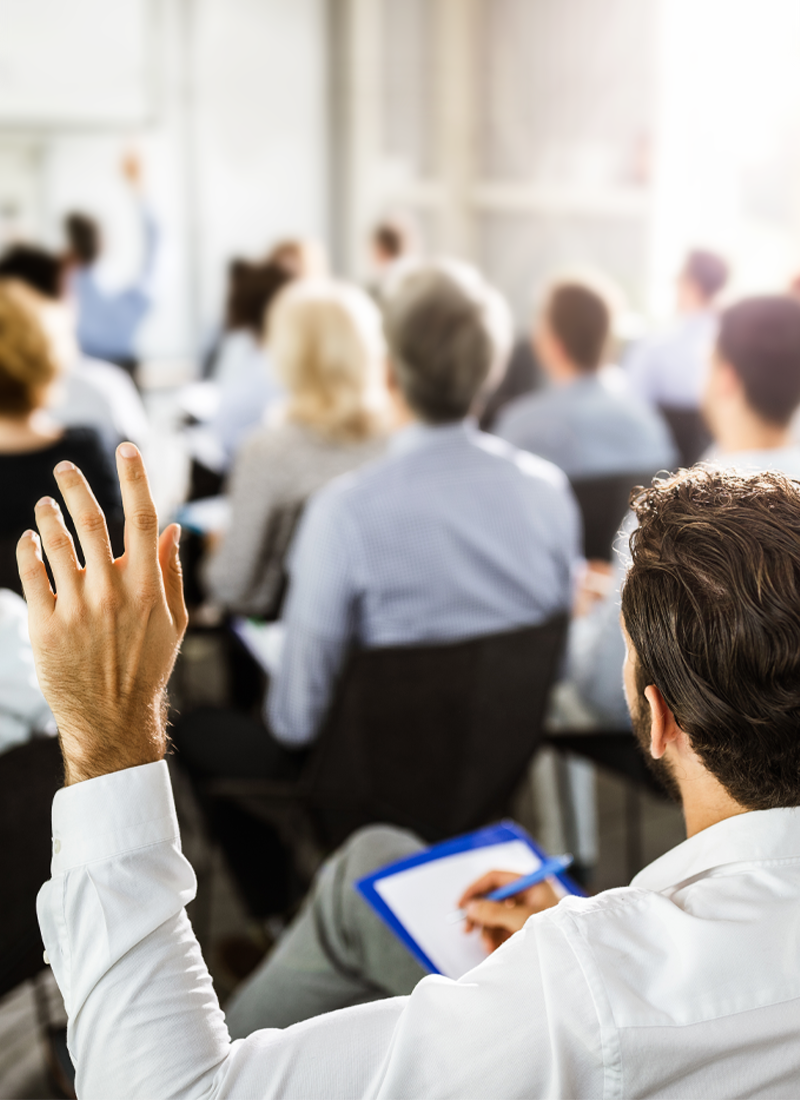 Mann hebt linke Hand zu einer Wortmeldung während einer Infoveranstaltung