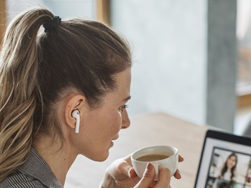 Treffen Sie envia TEL auf einer unserer Veranstaltungen. Frau sitzt mit einer Tasse Kaffee vor Laptop und nimmt an einer Webkonferenz teil