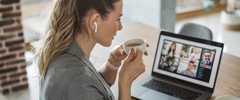 Treffen Sie envia TEL auf einer unserer Veranstaltungen. Frau sitzt mit einer Tasse Kaffee vor Laptop und nimmt an einer Webkonferenz teil