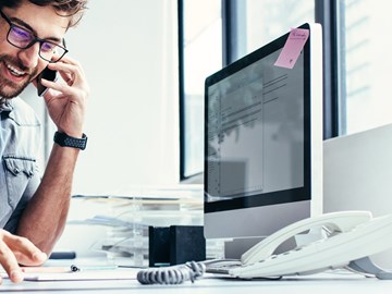 VoIP für Unternehmen Mann sitzt am Schreibtisch und telefoniert