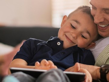 Gemeinsam surfen Vater und Sohn gemeinsam am Tablet, beide lachen zusammen