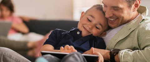 Gemeinsam surfen Vater und Sohn gemeinsam am Tablet, beide lachen zusammen