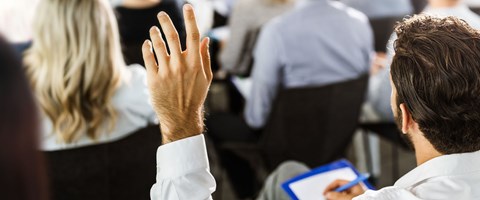 Die nächsten Infoveranstaltungen Mann hebt linke Hand für Wortmeldung während einer Veranstaltung