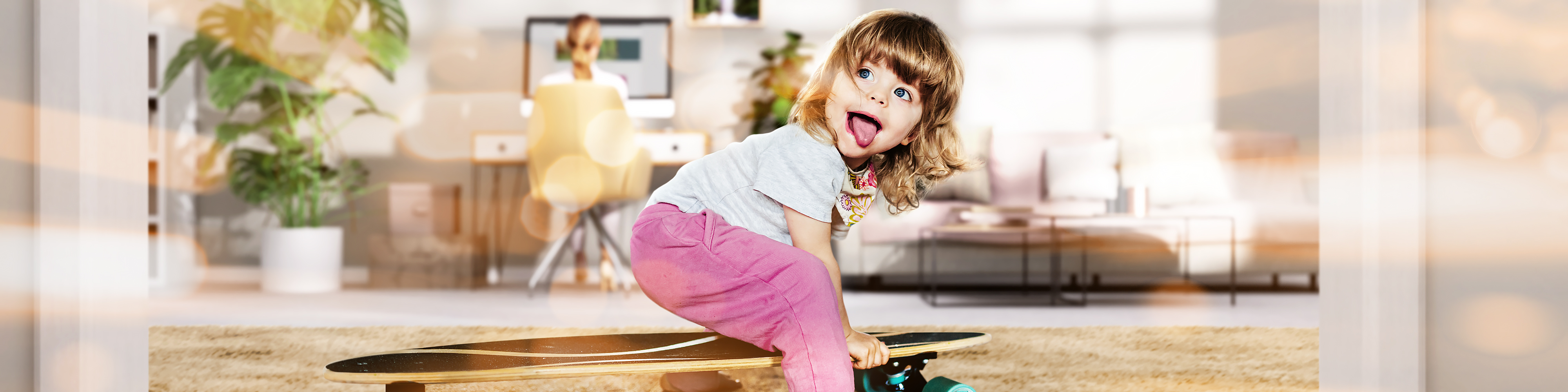 Kind spielt mit einem Skateboard, im Hintergrund die Mutter wie sie im Homeoffice arbeitet