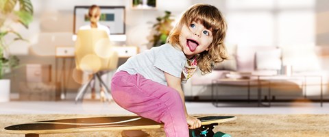 Privatkunden envia TEL Kind im Wohnzimmer sitzt auf einem Skateboard und streckt dabei die Zunge heraus