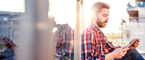 Wohnungswirtschaft-Produkte Mann sitzt auf einem Balkon und hält dabei ein Tablet in der Hand