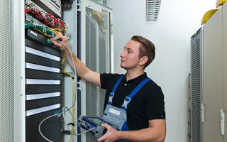 Azubi Elektroniker für Betriebstechnik Auszubildender vor einem Technikschrank im Rechenzentrum