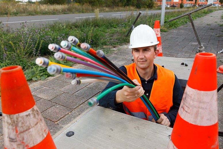 Schnelles Internet dank Glasfaser Ein Bauarbeiter, der eine Warnweste und einen Helm trägt, hält ein Glasfaserkabel in der Hand