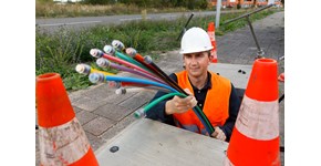 Schnelles Internet dank Glasfaser Ein Bauarbeiter, der eine Warnweste und einen Helm trägt, hält ein Glasfaserkabel in der Hand
