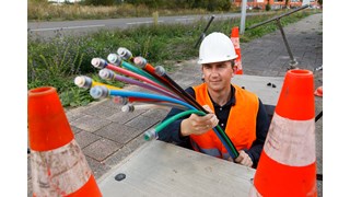 Schnelles Internet dank Glasfaser Ein Bauarbeiter, der eine Warnweste und einen Helm trägt, hält ein Glasfaserkabel in der Hand