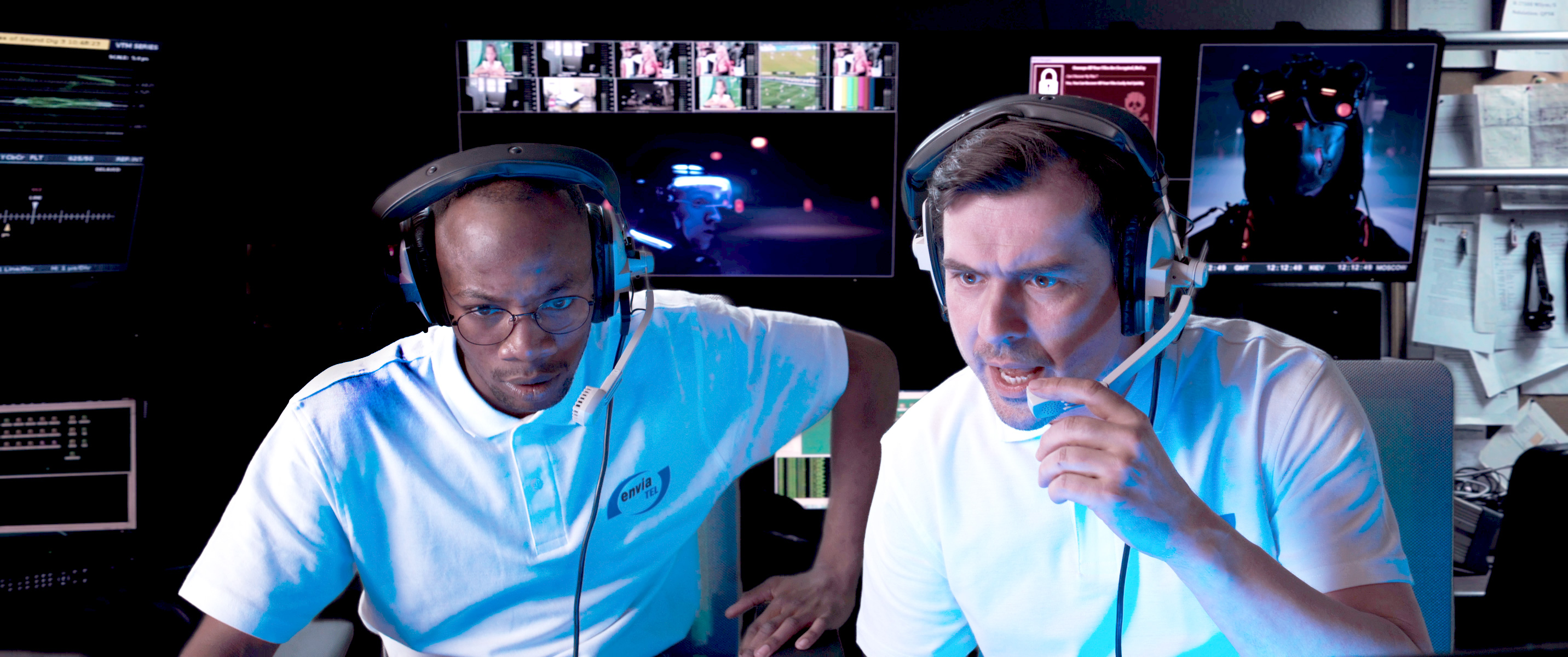 Zwei Männer mit envia TEL T-Shirts und Kopfhörern sitzen in einem Raum mit vielen Bildschirmen und überwachen Vorgänge