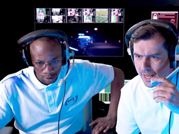 Security-Coaches envia-TEL Zwei Männer mit envia TEL T-Shirts und Kopfhörern sitzen in einem Raum mit vielen Bildschirmen und überwachen Vorgänge