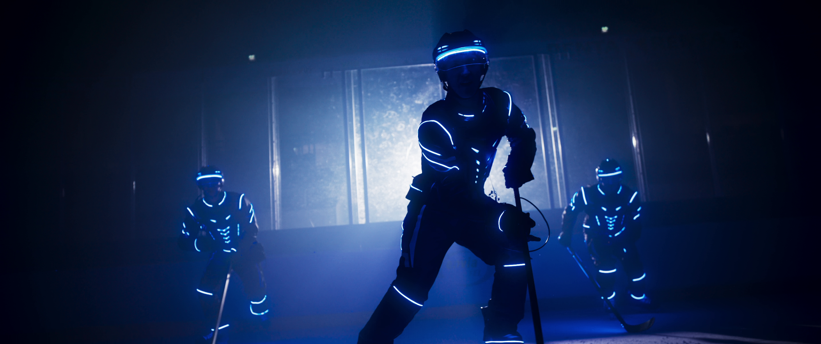 Drei Eishockeyspieler vor dunklem Hintergrund und blau beleuchteten Anzügen